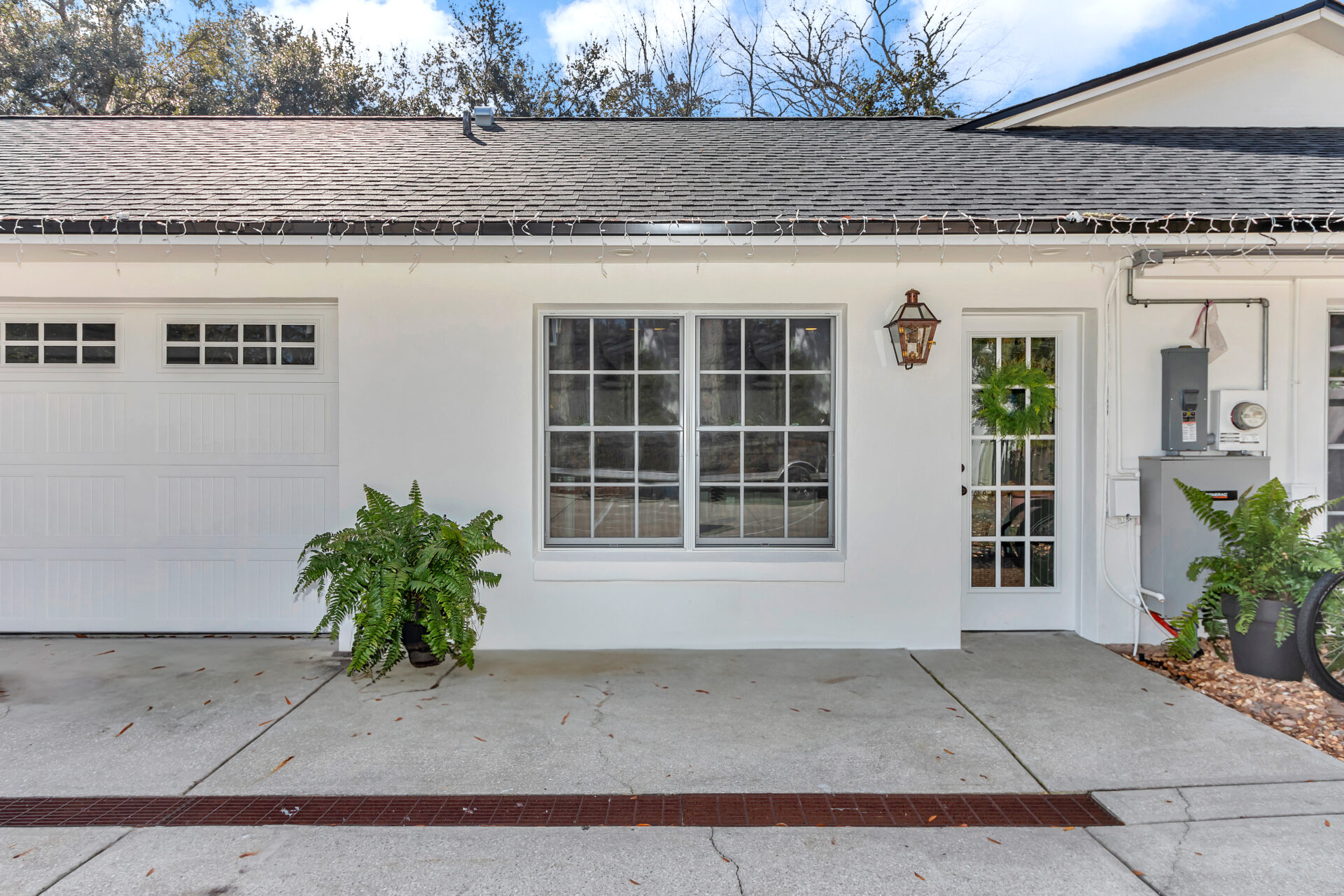 A welcoming front entrance featuring a white exterior, large windows, a decorative lantern, and a green wreath on the door, complemented by potted ferns.