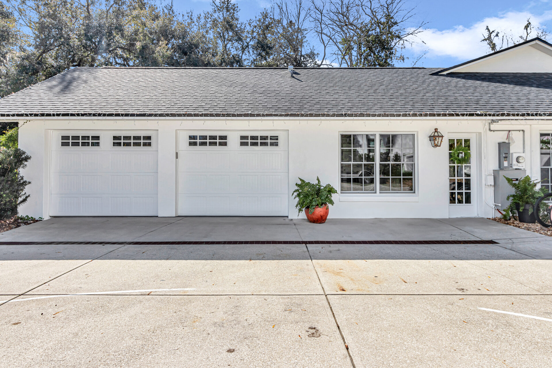 After Garage Conversion: A well-maintained white house exterior featuring two garage doors, a decorative lantern, and a vibrant planter with greenery in front, surrounded by a clean driveway and trees in the background.