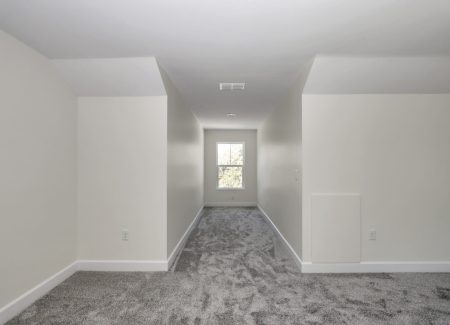 A long carpeted hallway within the finished attic, leading toward natural light from the shed row windows.