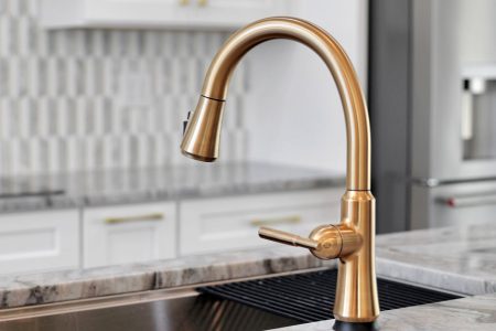 Close-up of a modern brushed gold kitchen faucet set against a sleek stainless steel undermount sink