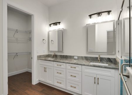 Grand master bathroom vanity with dual sinks, white cabinetry, and grey-veined granite countertops