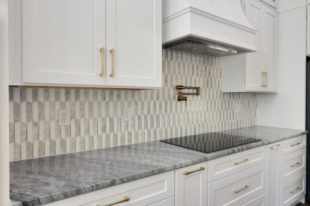 Intricate kitchen backsplash featuring a tiled arch pattern in white and grey with elegant gold trim accents