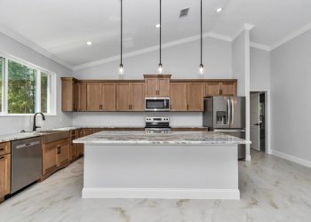 Large kitchen island with white and grey marble-patterned granite countertop and custom wood cabinetry, central to this home design - home designs with mother in law suites