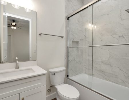 Private en-suite bathroom for the third bedroom, featuring a bathtub with modern glass gliding doors and granite walls