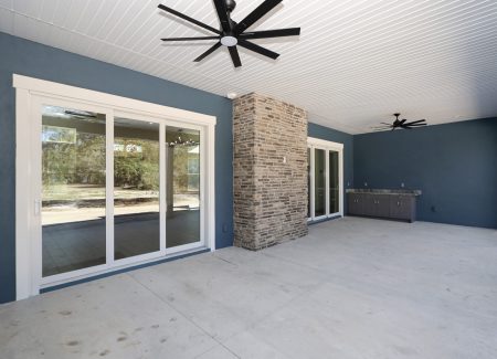 Spacious covered lanai featuring bold blue exterior siding, dual cooling fans, and a high-end outdoor living layout.