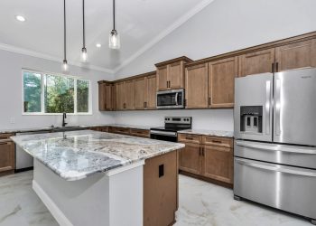 Spacious custom kitchen in the French Residence featuring warm wood cabinets, white and grey marble-patterned granite countertops, and a large island - home designs with mother in law suites