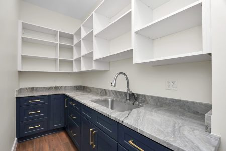 Spacious walk-in pantry room behind the kitchen, featuring floor-to-ceiling white open-faced cabinetry and a blue base cabinet.