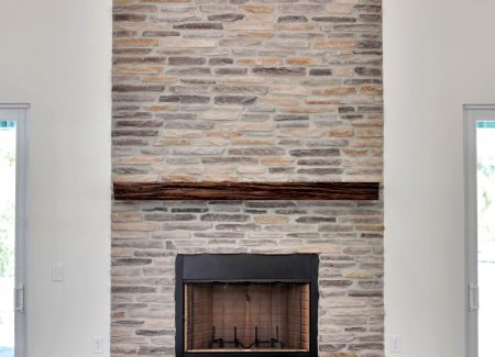 Stunning floor-to-ceiling multicolor stone fireplace in the great room, featuring a rustic real wood mantle and antler chandelier.