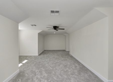 Expansive finished attic bonus room with plush grey carpeting and natural light, built by a leading custom home builder in Ocala, FL.