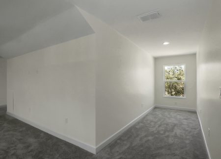 View of the second long hallway in the finished attic, leading toward a single-pane window and bright grey-carpeted living space.