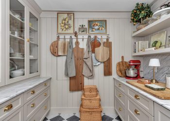 A beautifully designed kitchen corner featuring wooden cutting boards, aprons, and decorative elements against a light-colored wall, complemented by elegant cabinetry and marble countertops.