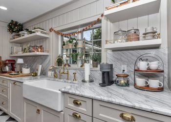 Stylish kitchen featuring marble countertops, brass fixtures, and a farmhouse sink, adorned with plants and decorative accents.