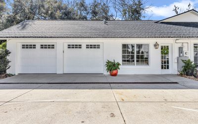After Garage Conversion: A well-maintained white house exterior featuring two garage doors, a decorative lantern, and a vibrant planter with greenery in front, surrounded by a clean driveway and trees in the background.